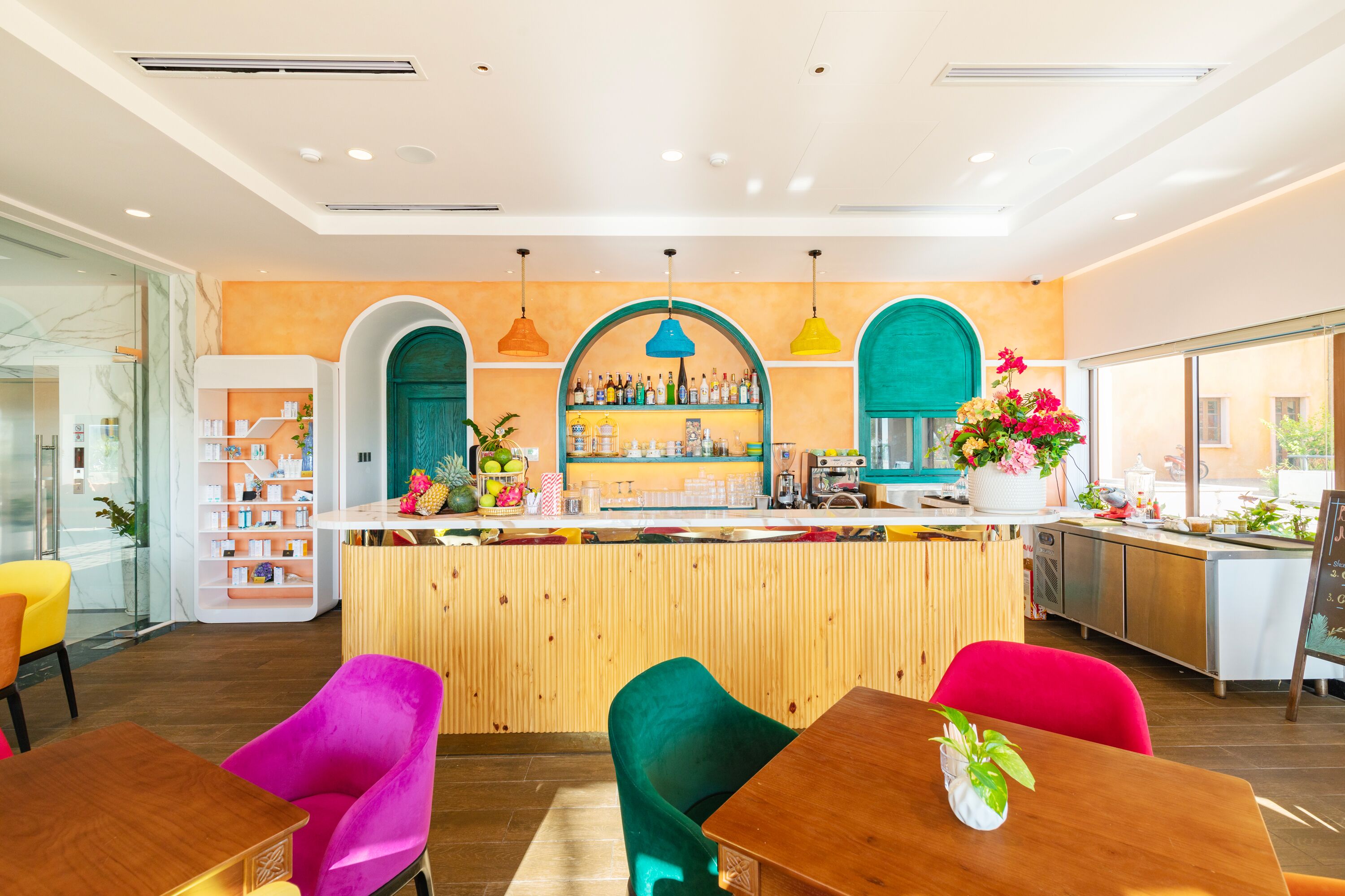 Zona bar moderna con bancone in legno, sedie colorate e una varietà di bottiglie e decorazioni.
