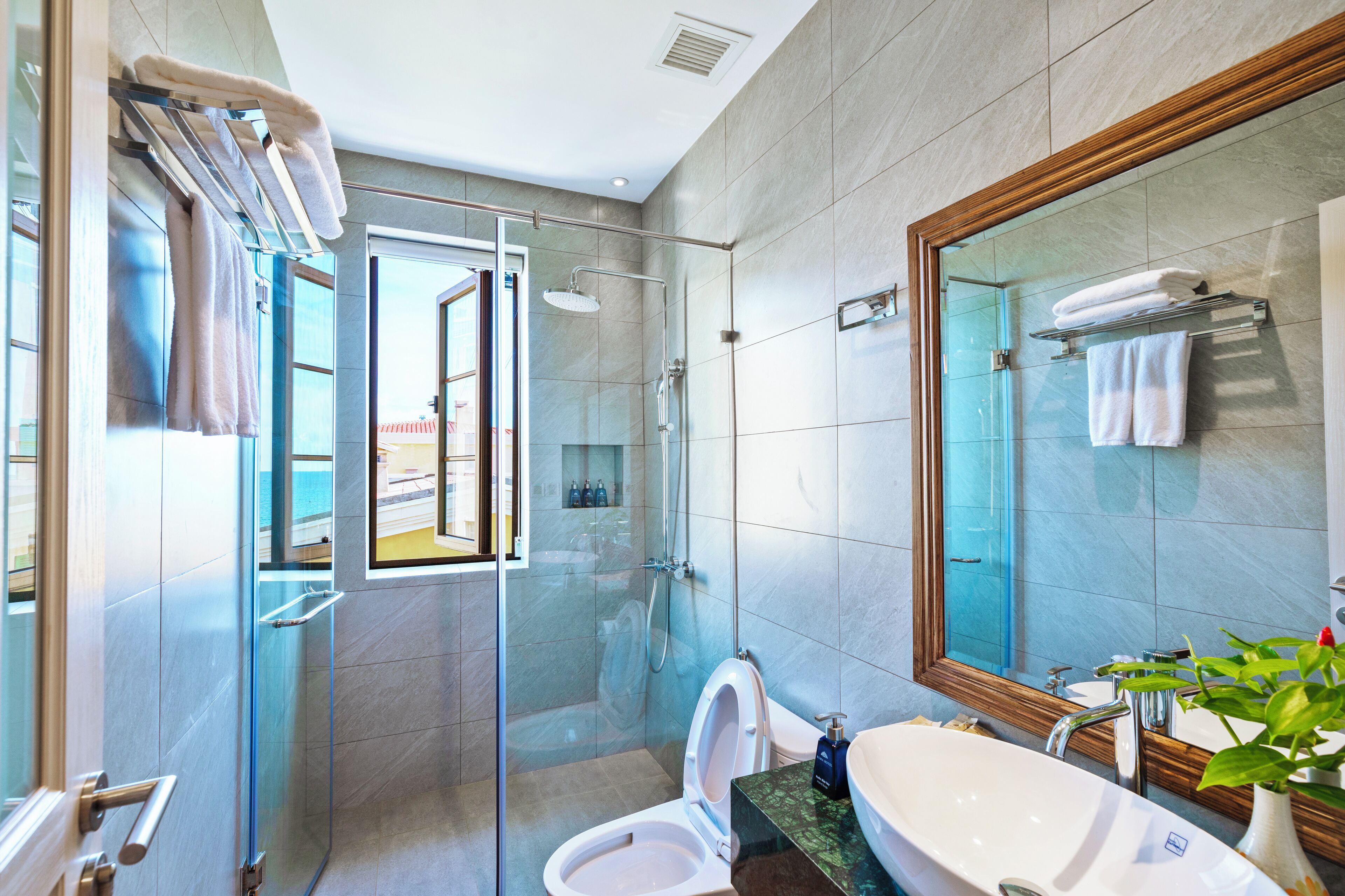 A modern bathroom with a glass-enclosed shower, a white toilet, a sink with a marble countertop, and a large mirror.