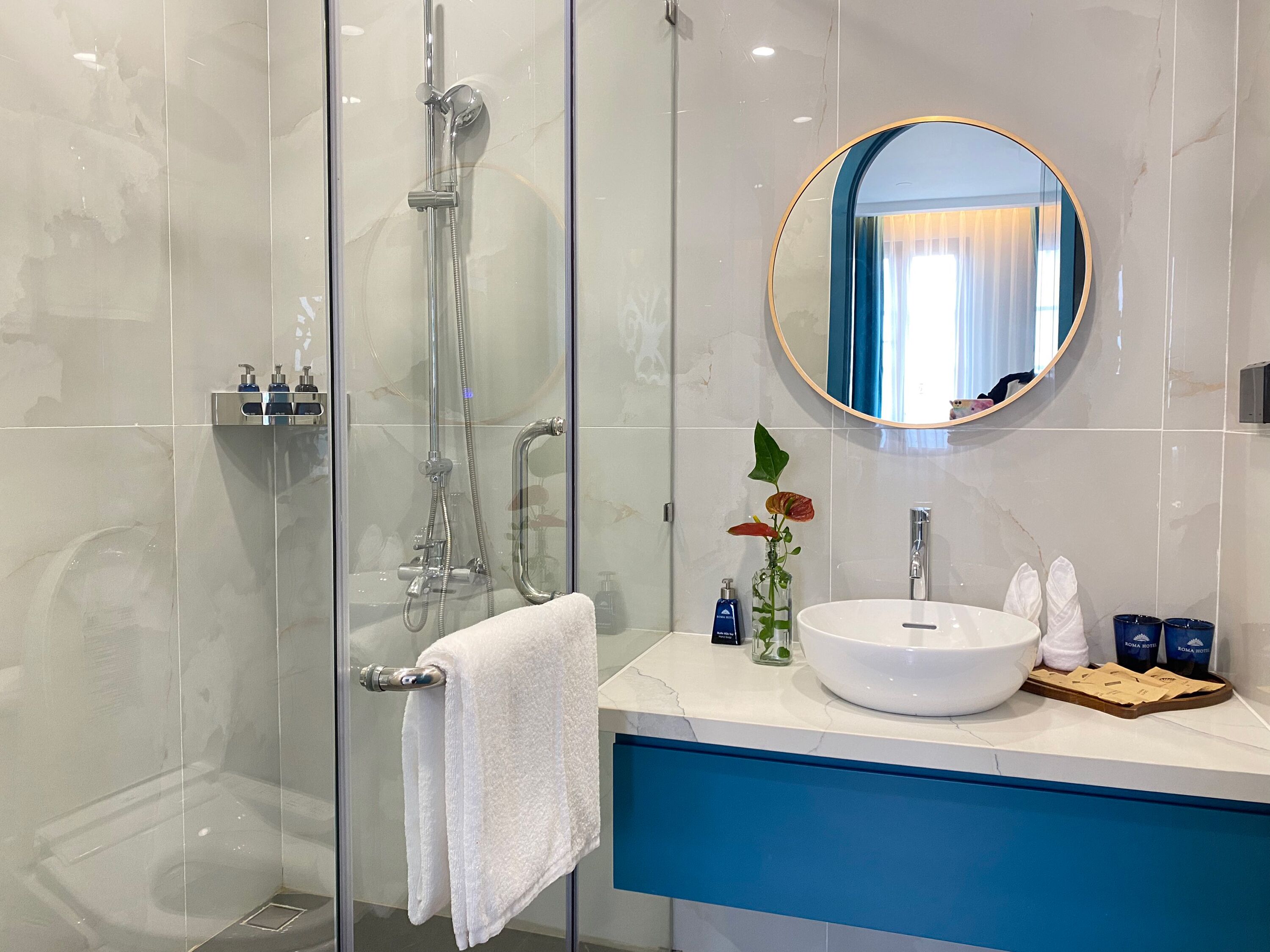 A modern bathroom with a glass-enclosed shower, a white sink with a round mirror, and a blue countertop.
