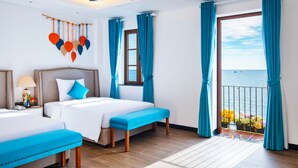 A hotel room with a bed, a bench, a ceiling fan, a window with curtains, and a view of the sea.