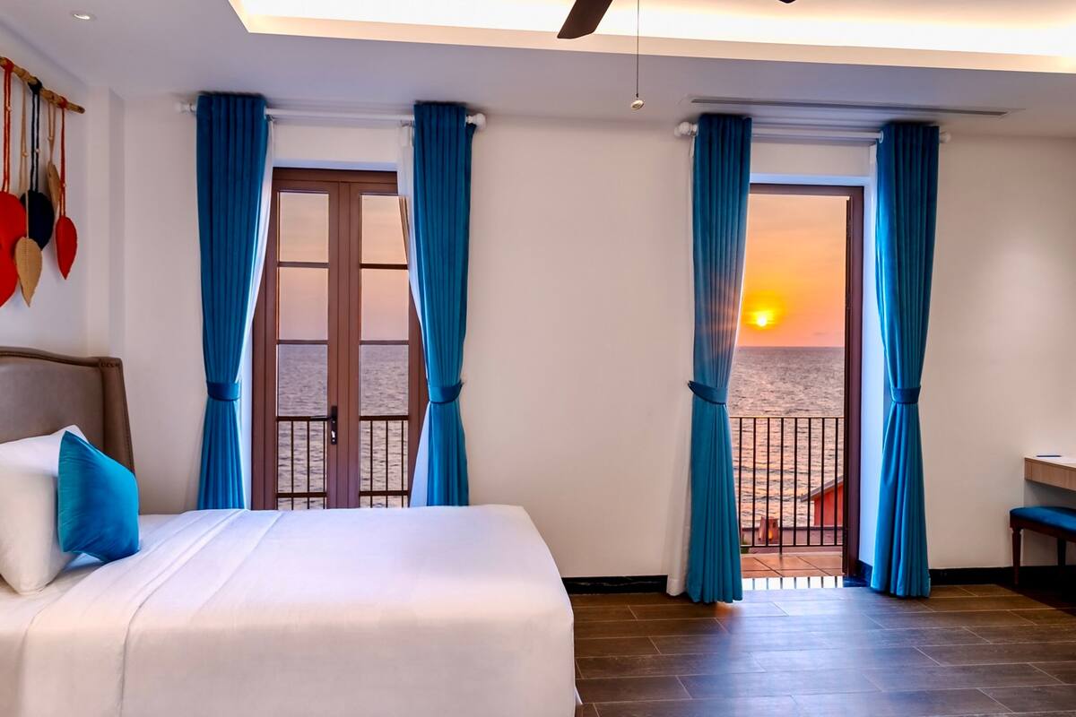 Un dormitorio con cama, escritorio y vista al atardecer sobre el mar.