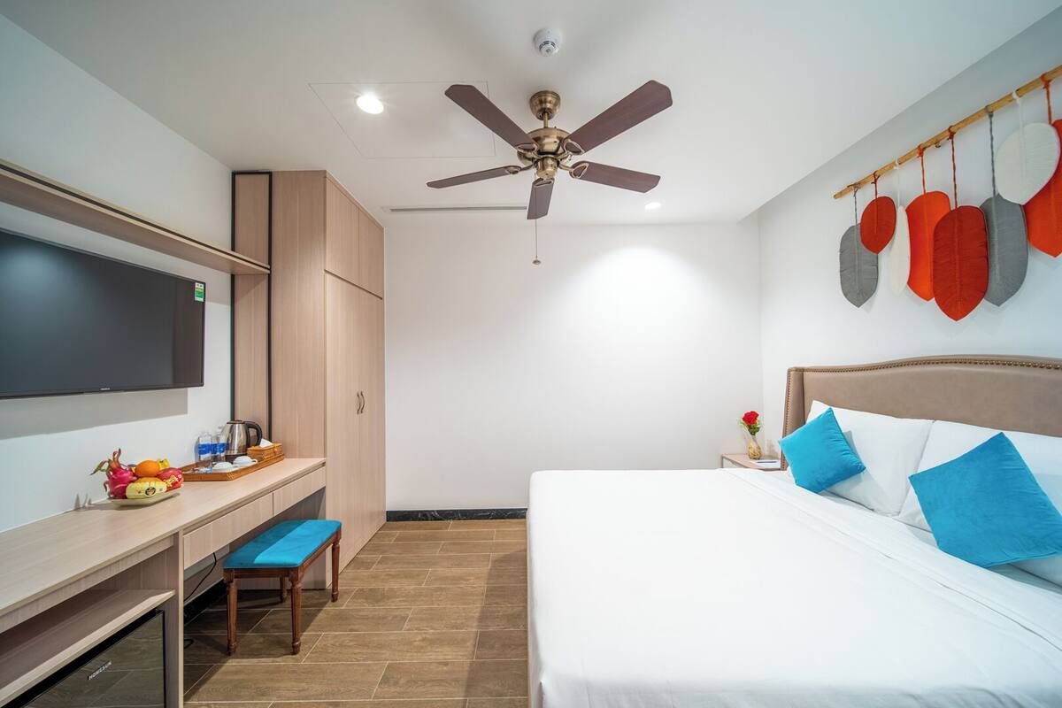 Una habitación de hotel con una cama, un escritorio, un televisor, un ventilador de techo y una decoración en la pared.