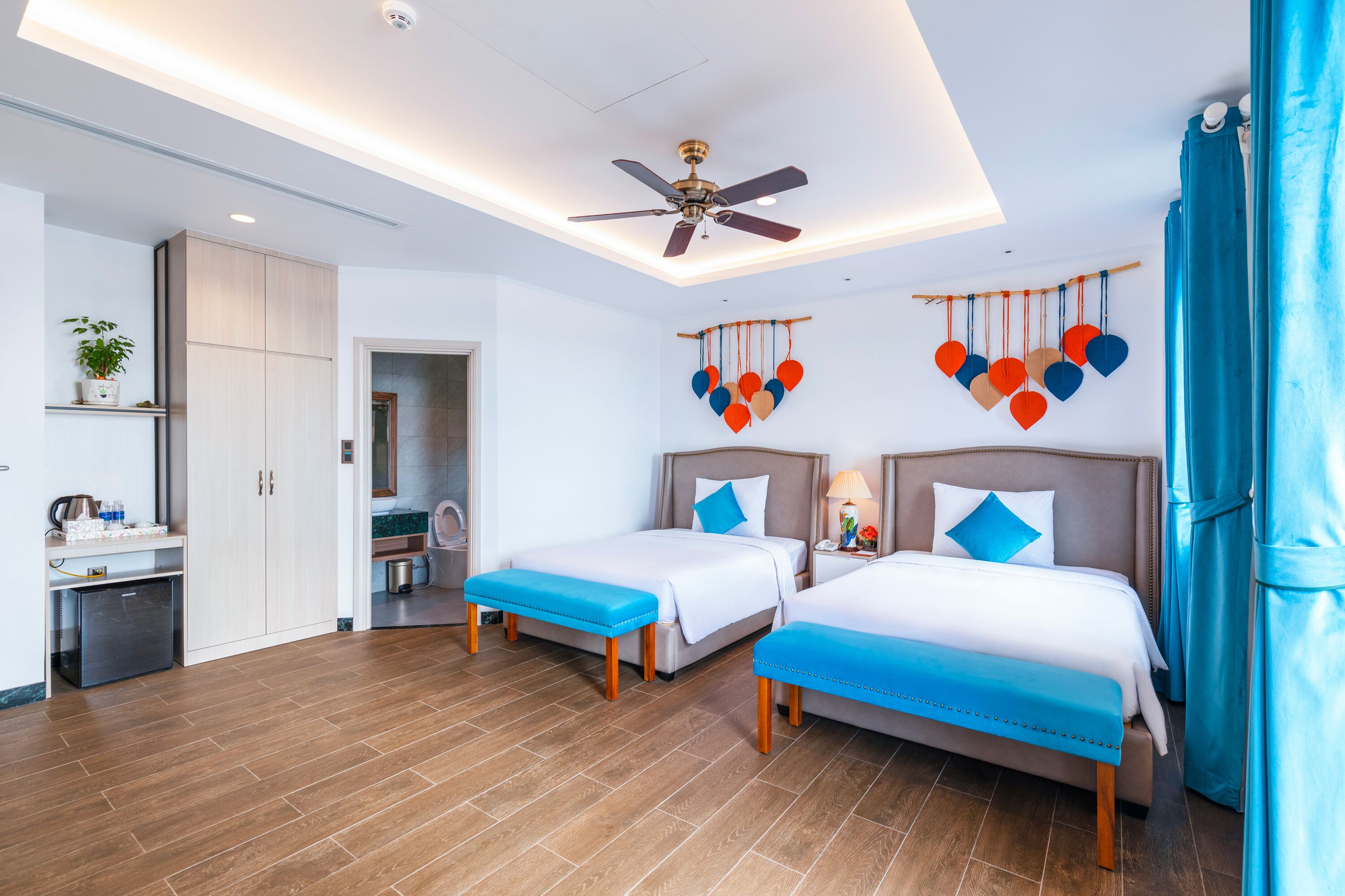 A hotel room with two beds, a ceiling fan, a small kitchenette, and a bathroom visible through an open door.