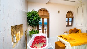 A modern bathroom with a bathtub filled with rose petals, a shower area, and a bed with a yellow bedspread.