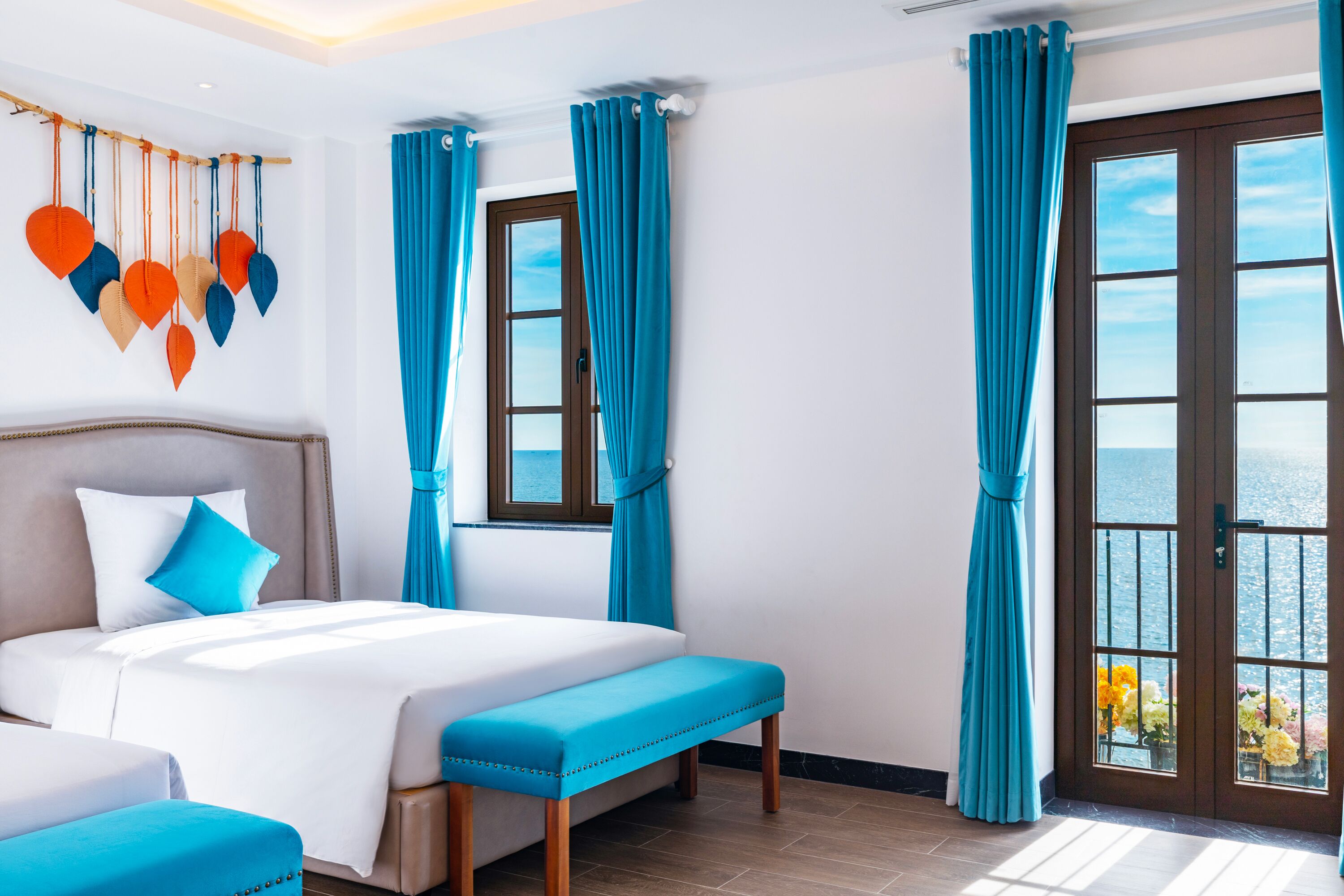 A hotel room with a large bed, a bench, a view of the sea, and a window with curtains.