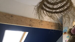 A bedroom with a sloped ceiling, a skylight, a bed with striped bedding, a teddy bear, and a woven basket.