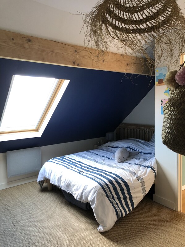 A bedroom with a sloped ceiling, a skylight, a bed with striped bedding, a teddy bear, and a woven basket.