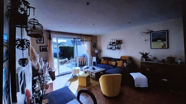 A living room with a sofa, armchairs, a coffee table, and a dining table. There is a large window with curtains, a lamp, and a framed picture on the wall.