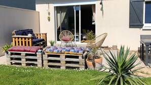 A patio with a wooden bench, a wicker chair, and a potted plant.
