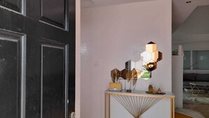 Un interior moderno con una puerta negra, una consola blanca de diseño geométrico y una lámpara fijada a la pared.