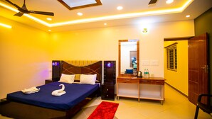 A hotel room with a bed, a desk, a chair, a ceiling fan, and a red rug. - Queens Paradise Estate (Vanur)