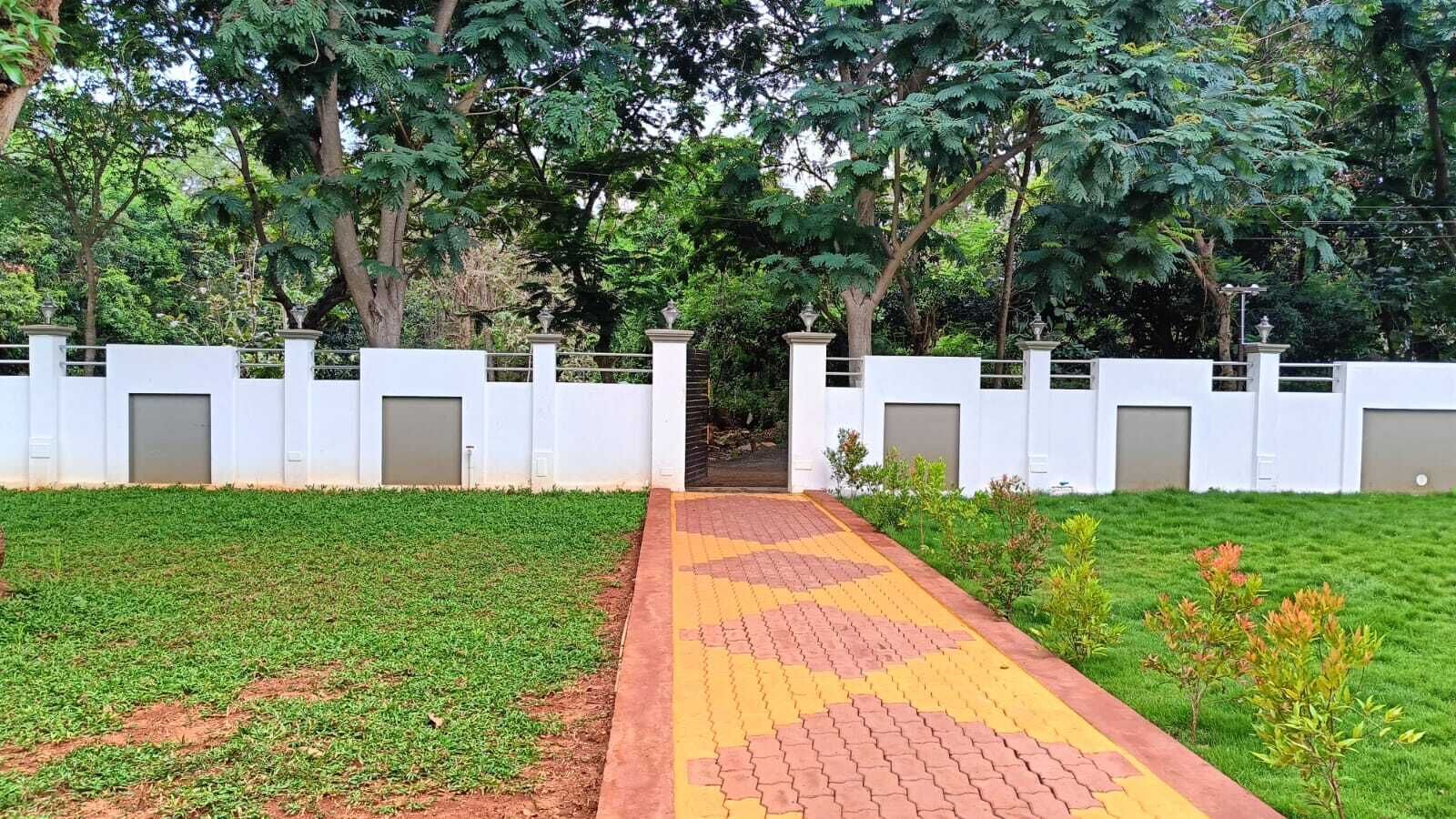 A pathway leading to a gated entrance with a white fence and trees in the background.