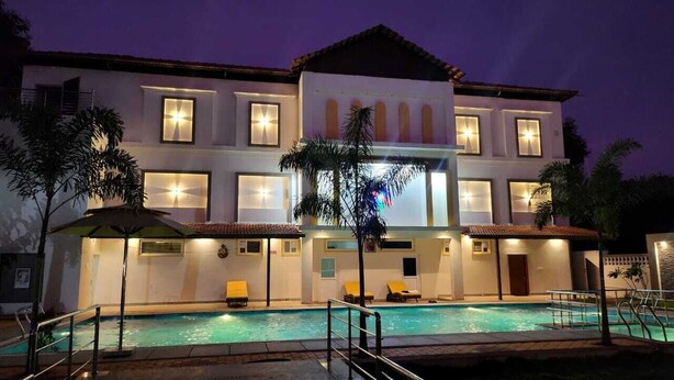 A two-story building with a swimming pool, multiple windows, and outdoor seating. - Queens Paradise Estate (Vanur)