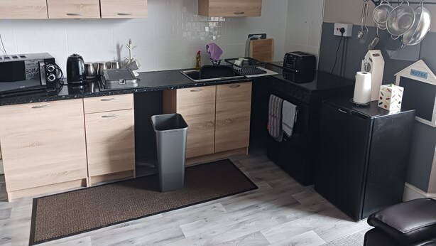 Una cucina compatta con mobili in legno, un piano di lavoro nero e un frigorifero nero.