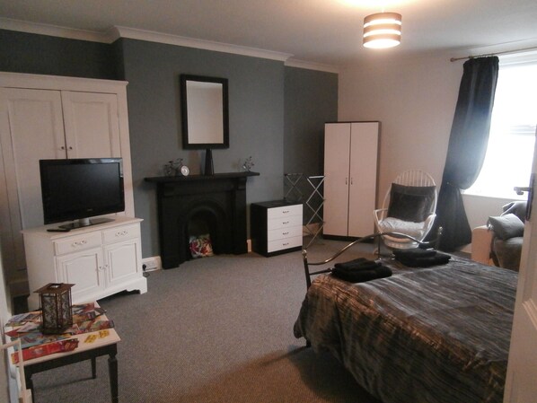 A bedroom with a bed, a television on a dresser, a fireplace, a wardrobe, and a chair. - Charming Seafront 2-bed Apartment in Llandudno (Llandudno)