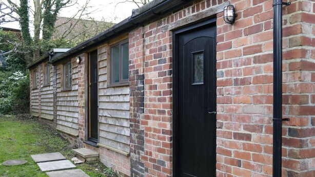 A brick building with a black door and windows, stone steps leading to the entrance, and daffodils at the base. - a Quirky Garden Building in an Orchard (Ryton)
