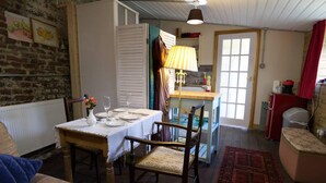 A cozy dining area with a table set for two, a wooden chair, and a kitchen area with a sink and cabinets. - a Quirky Garden Building in an Orchard (Ryton)