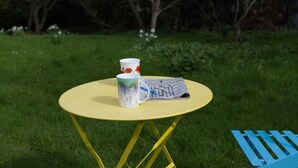 A yellow folding table with a white mug and a newspaper on it, set on grass. - a Quirky Garden Building in an Orchard (Ryton)