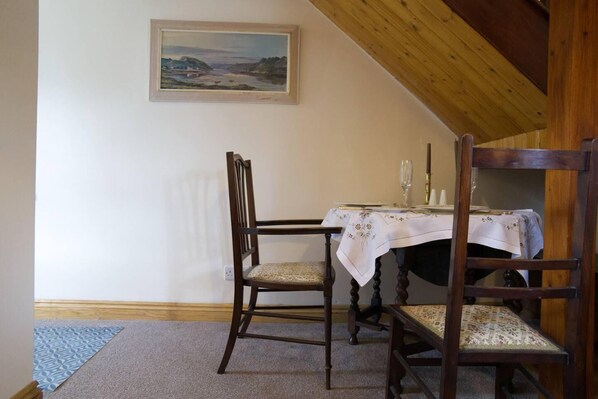 A dining area with two wooden chairs, a table with a white tablecloth, and a painting on the wall. - Cottage - Sleeps 2 - Garden - Parking (Ryton)