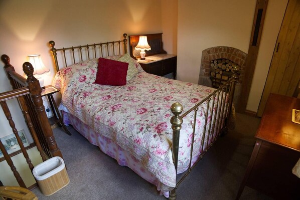 A bedroom with a bed, bedside lamps, a chair, a nightstand, and a fireplace.