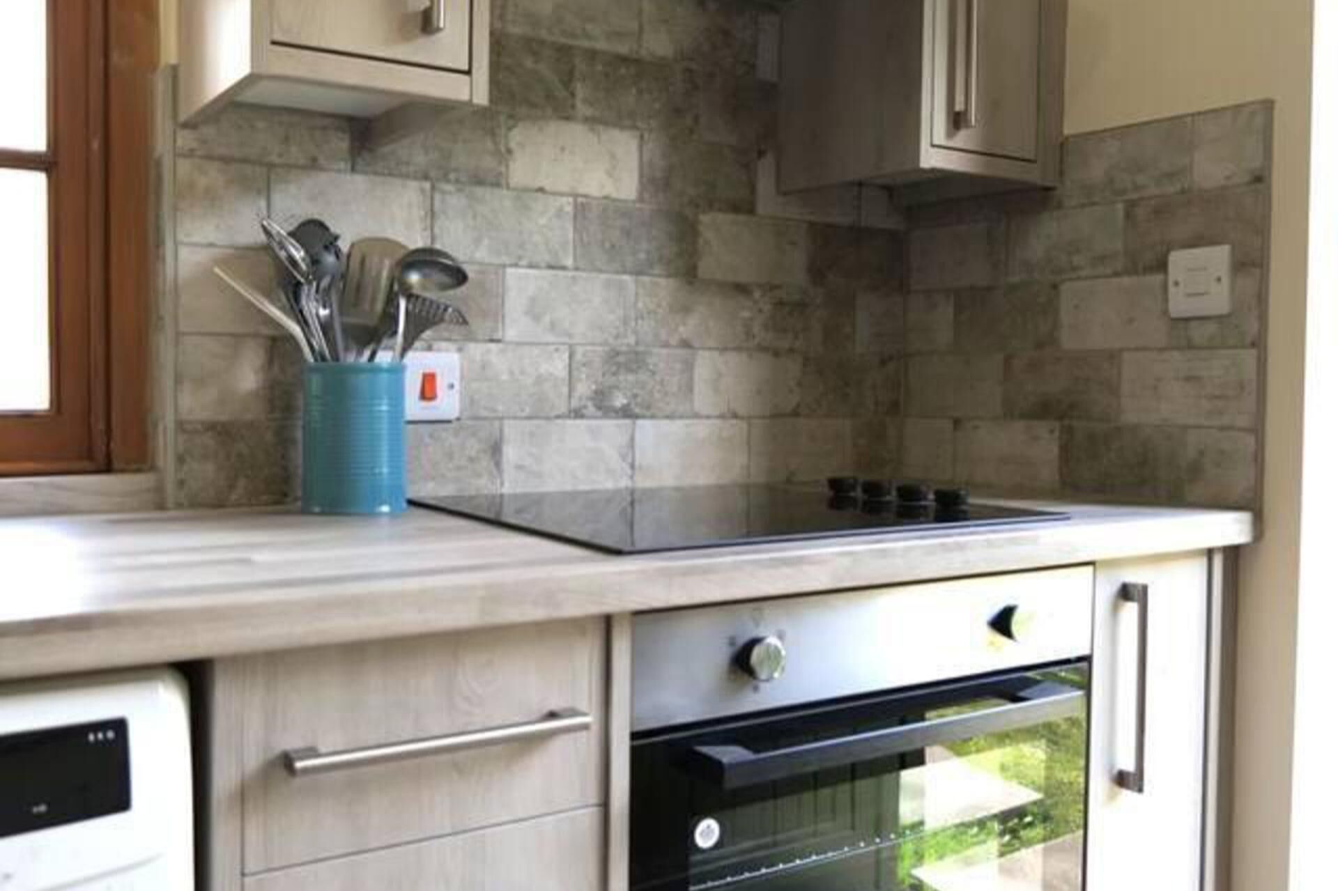 A kitchen with a stone backsplash, a built-in oven, and a blue utensil holder.