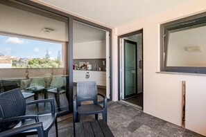 A balcony with a glass door leading to a kitchen area, a dining table with chairs, and a view of the outside. - Spacious Seaside apartment A - Faraway (Lagoa)