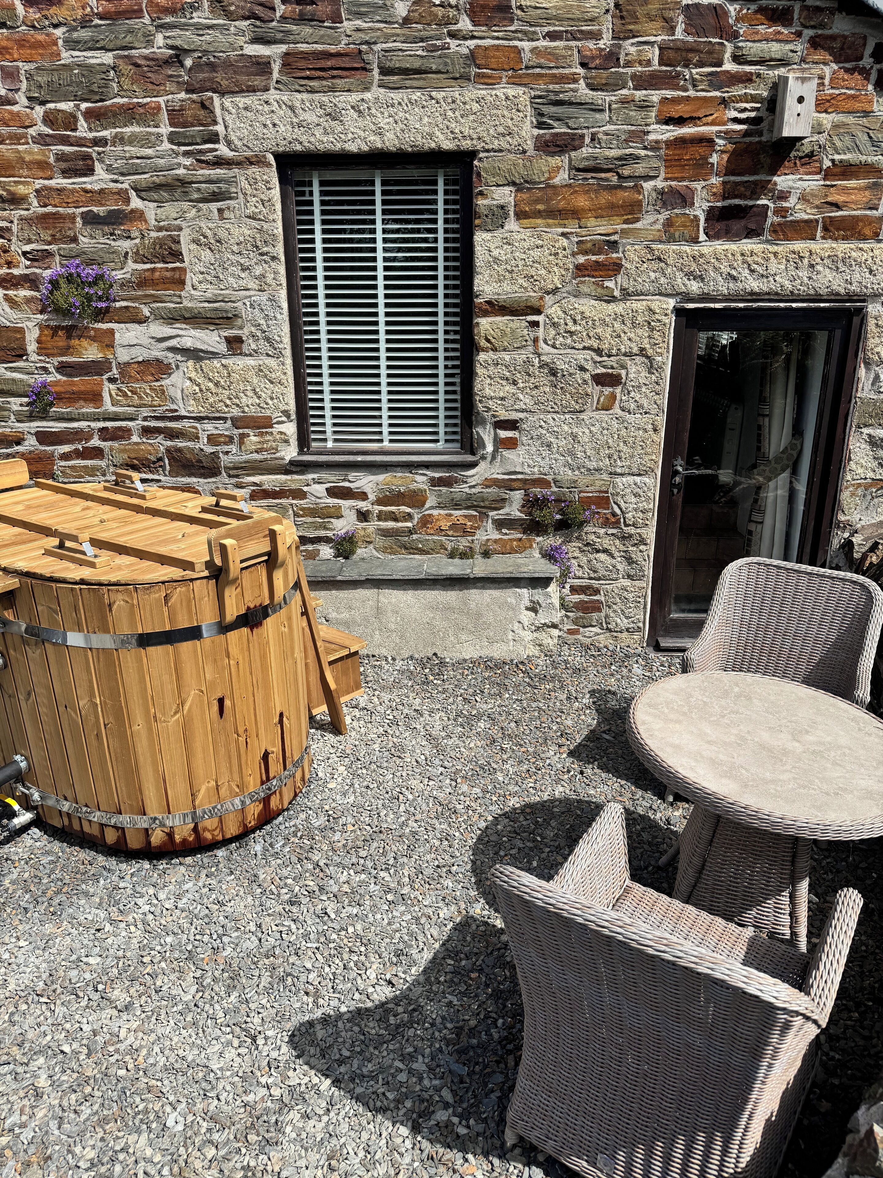 A stone building with a wooden barrel, wicker chairs, and a table.