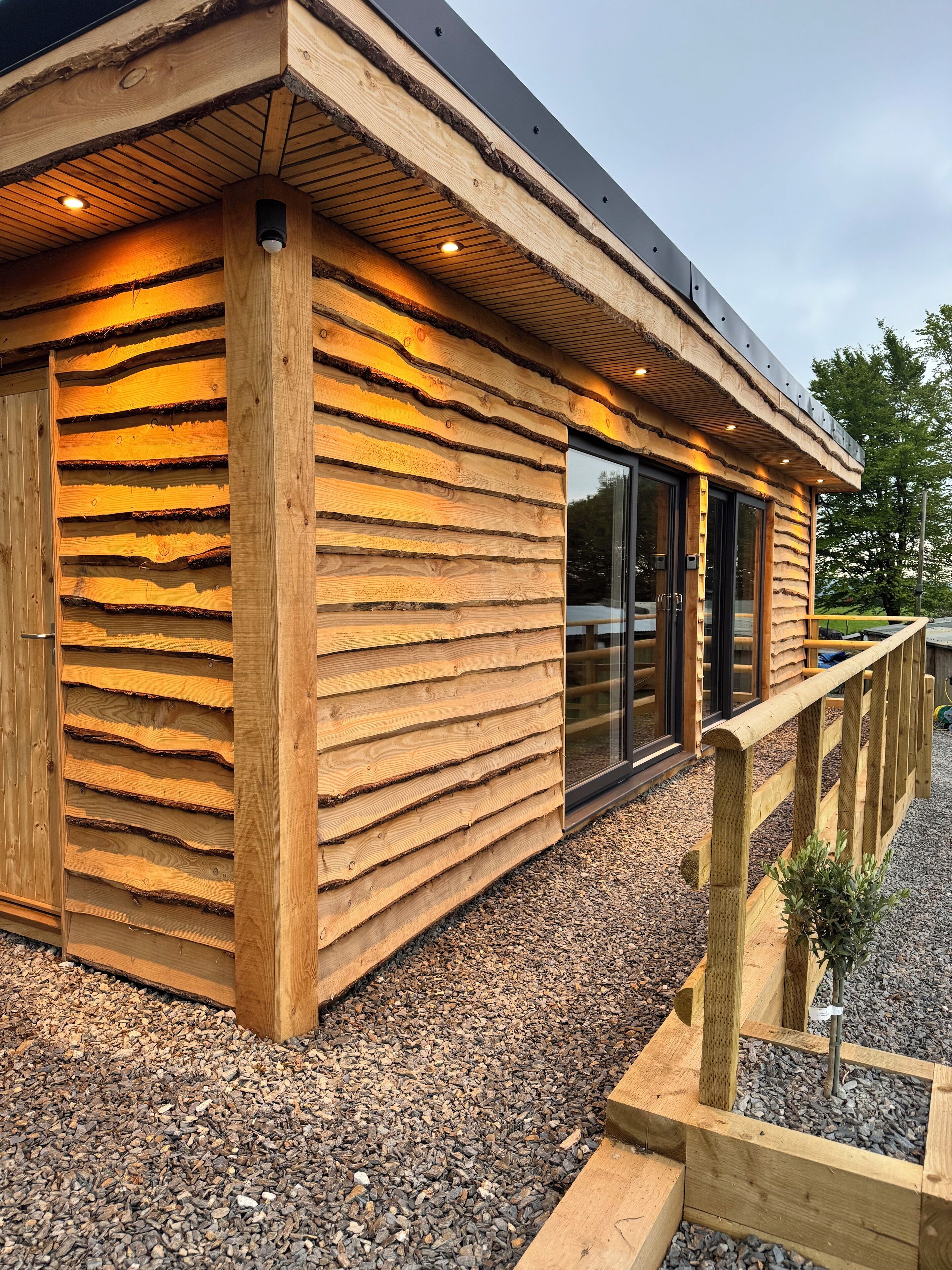A wooden cabin with a sloped roof, large windows, and a gravel driveway.