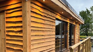 A wooden cabin with a sloped roof, large windows, and a gravel driveway. - Nuthatch - Traditional Cornish Stone Cottage (Bodmin)