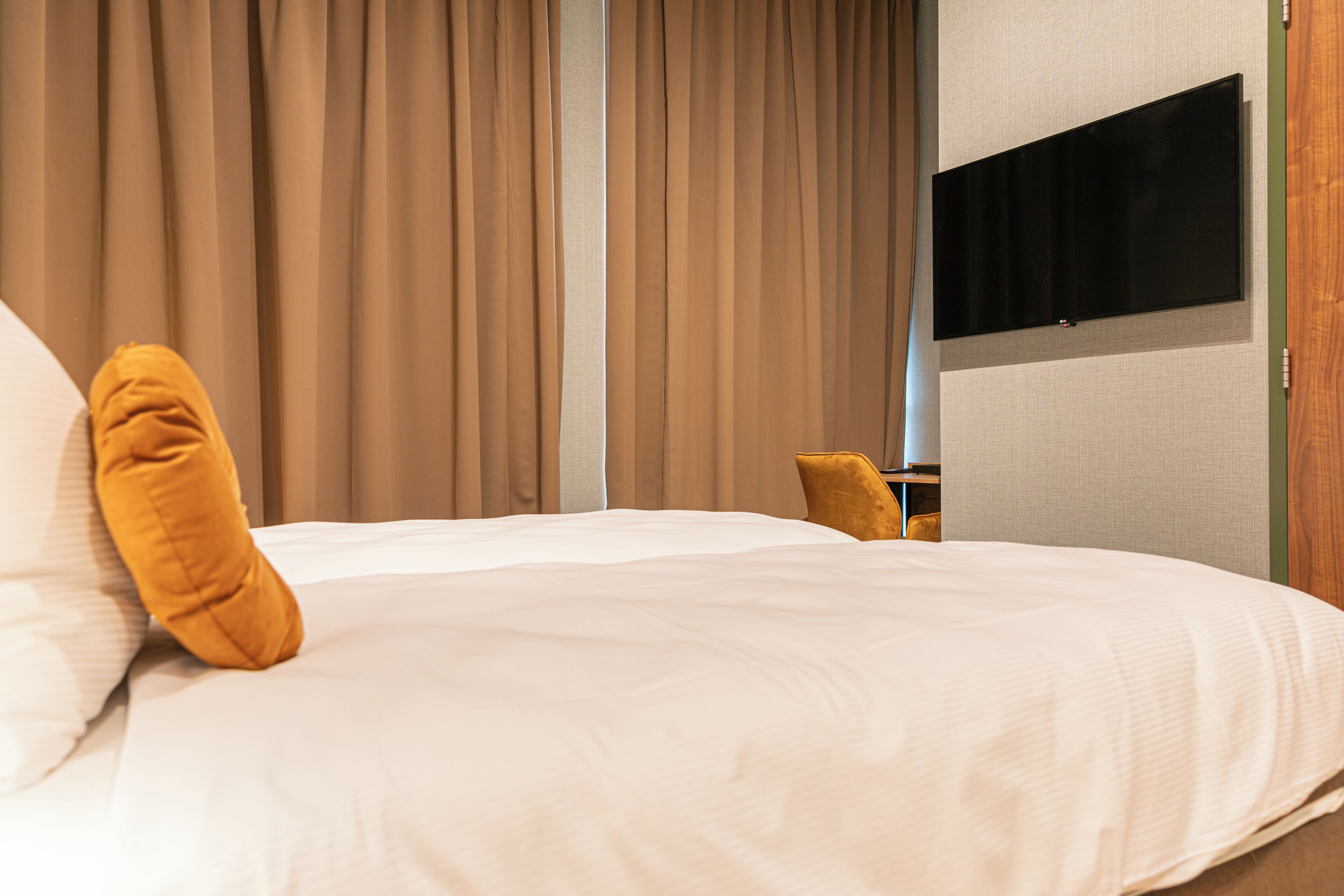 Quarto de hotel com uma cama, uma televisão fixada na parede e uma janela com cortinas.