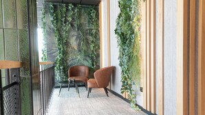 A corridor with a wooden floor, two brown armchairs, a small table, and a wall decorated with green plants. - Distrikt Hotels Amsterdam Zaandam  (Zaandam)