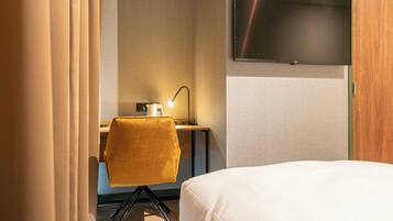 Ein Hotelzimmer mit einem Bett, einem Schreibtisch mit Stuhl, einem an der Wand befestigten Fernseher und einer Schreibtischlampe.
