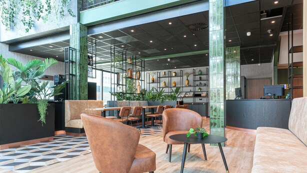 A modern lobby with seating areas, a reception desk, and a large window with greenery. - Distrikt Hotels Amsterdam Zaandam  (Zaandam)