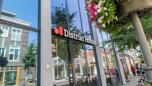 A building with a glass facade, a visible entrance, and a hanging flower basket. - Distrikt Hotels Amsterdam Zaandam  (Zaandam)