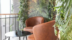 A seating area with two brown leather chairs and a small round table, surrounded by lush green plants and a textured wall. - Distrikt Hotels Amsterdam Zaandam  (Zaandam)