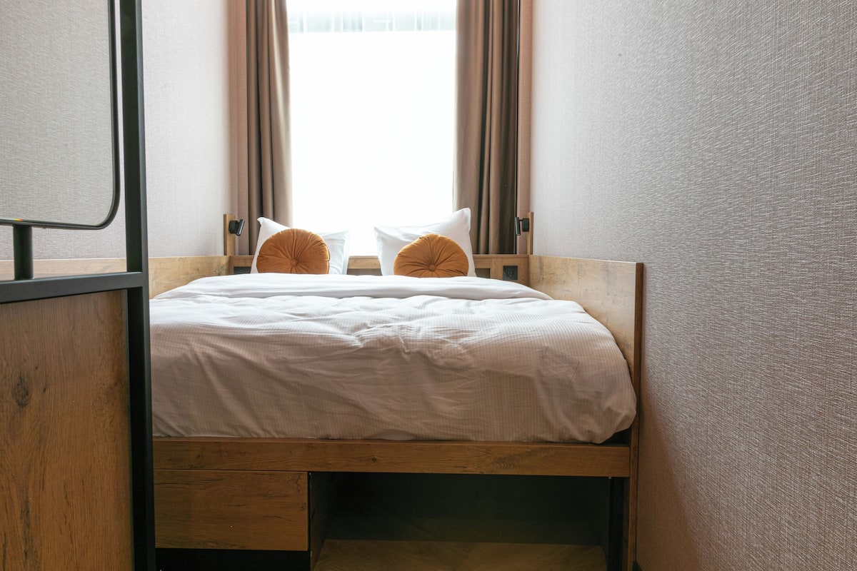 A single bed with a wooden frame, white bedding, and two orange pillows.