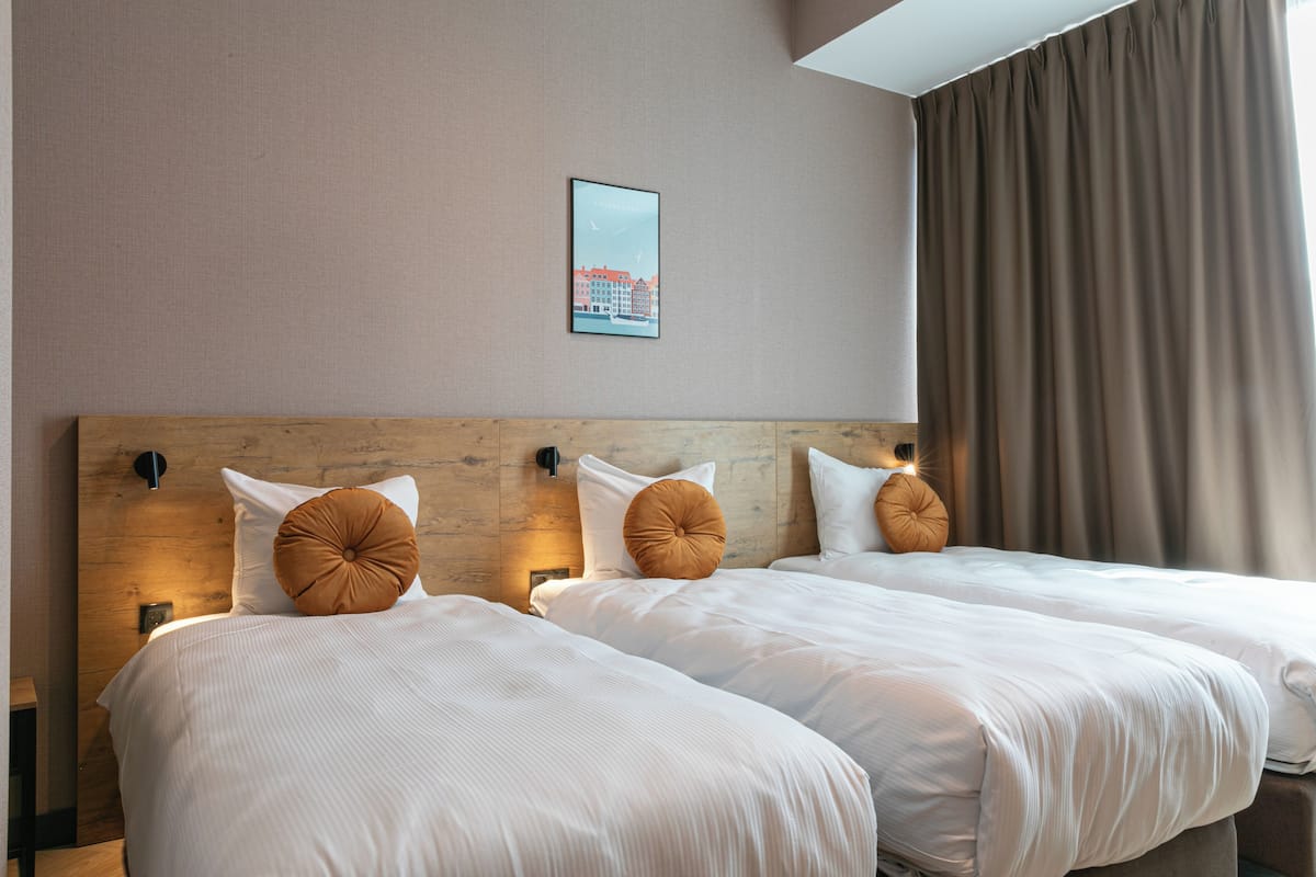 A hotel room with two beds, a headboard, a framed picture on the wall, and a window with curtains.