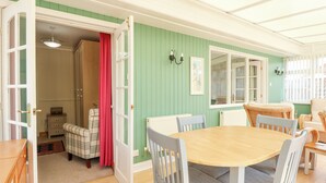 Un coin repas avec une table ronde en bois et six chaises, un rideau rouge et un mur vert.