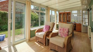 Une véranda meublée de mobilier en osier, dotée de grandes fenêtres et offrant une vue sur le jardin.