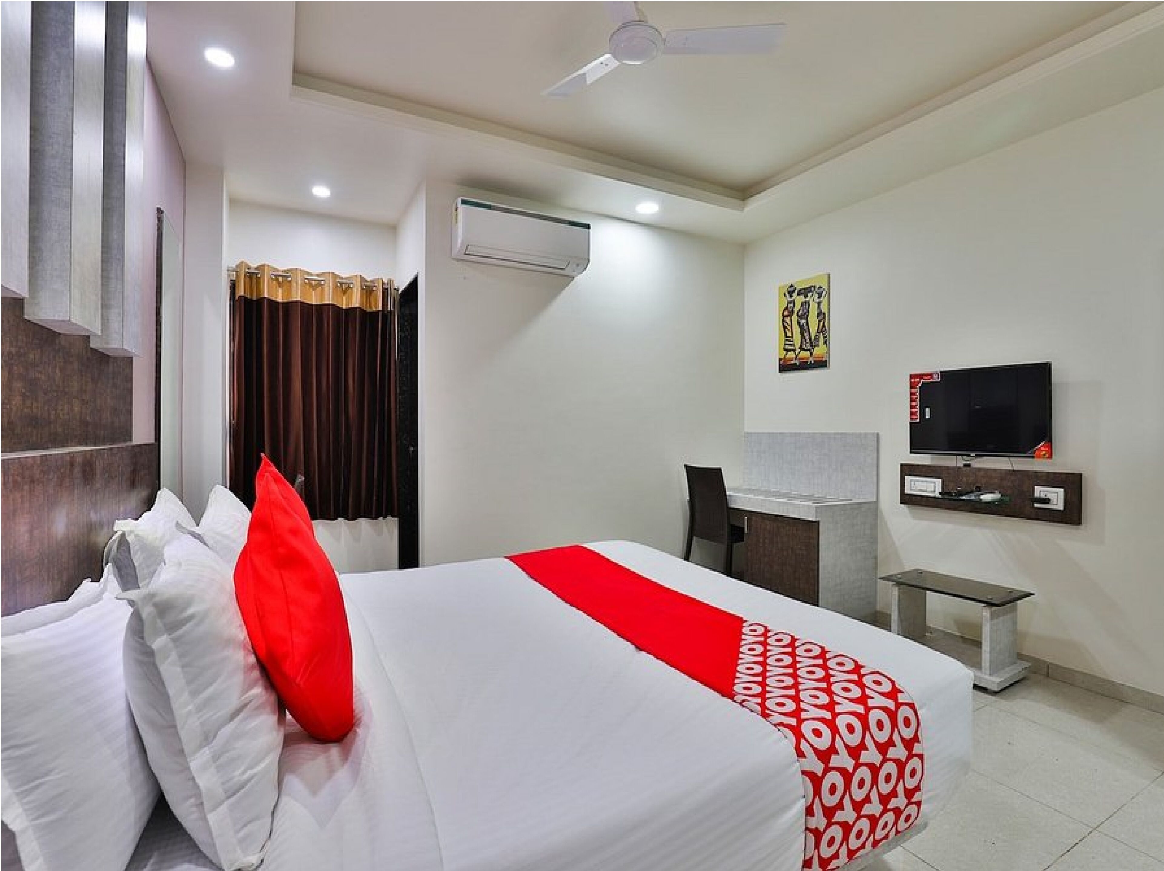 A hotel room with a bed, a desk, a chair, a TV, and an air conditioning unit.