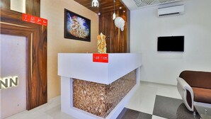 Een receptiegedeelte met een houten receptiebalie, een ingelijst schilderij erboven, een witte tv aan de muur en een bruine leren bank.