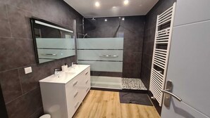 Une salle de bain moderne avec un meuble-lavabo blanc, une cabine de douche en verre et une douche à l’italienne.