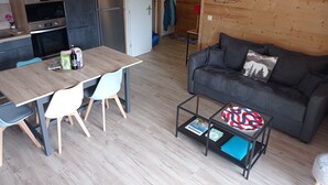 Un espace de vie moderne avec un plancher en bois, un canapé gris foncé, une table à manger en bois avec des chaises, une machine à café et un luminaire suspendu.