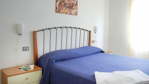 A bedroom with a wooden headboard, a blue bedspread, a white pillow, and a nightstand with a lamp and a book. - Residence Belvedere (Ascea)