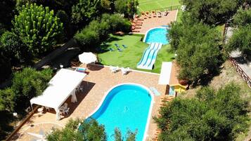 An aerial view of a resort with a large swimming pool, a water slide, and a tennis court.