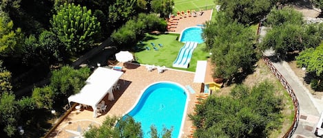 Vista aérea de um resort com uma grande piscina, um tobogã aquático e uma quadra de tênis.