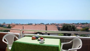 A balcony with a table set for tea, overlooking a coastal town with terracotta rooftops. - Residence Belvedere (Ascea)