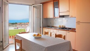 A kitchen with a view of the sea, a dining table with fruit, and a balcony with a table and chairs. - Residence Belvedere (Ascea)