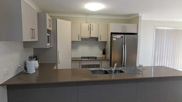 A modern kitchen with a central island, stainless steel appliances, and a tiled floor. - Gladstone Super Home Fully Fenced With Central Aircondioning (New Auckland)