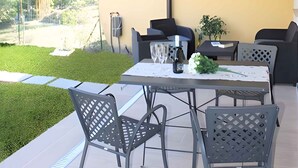 Eine Terrasse im Freien mit einem für zwei Personen gedeckten Tisch, umgeben von Stühlen, unter einer gestreiften Markise.